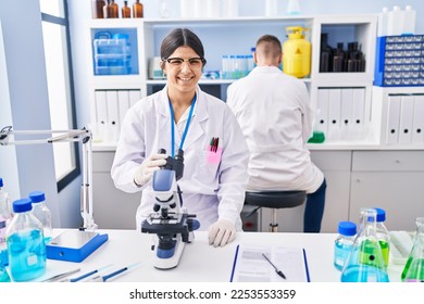 Young woman working at scientist laboratory looking positive and happy standing and smiling with a confident smile showing teeth  - Shutterstock ID 2253553359