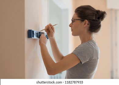 Young Woman Working With A Spirit Level And Drawing On A Wall, Home Renovation And Construction Concept