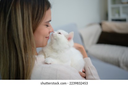 A young woman works at home while a white Persian cat snuggles alongside to encourage his master
