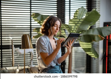 Junge Frau arbeitet auf einem Touchpad und fühlt sich in einem gemütlichen Hausbüro mit einer grünen Pflanze auf dem Hintergrund wohl