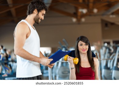 Young woman works out with dumbbells as her trainer supervises in a fitness center - Powered by Shutterstock