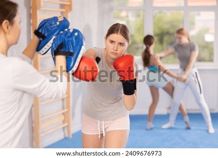 Young woman works out strength and speed of boxing punch mitts with help of female coach partner in boxing paws. Woman performs role of target and mannequins during training strike technique Stock photo © 