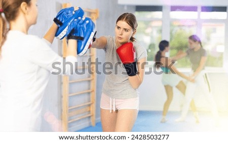 Young woman works out strength and speed of boxing punch mitts with help of female coach partner in boxing paws. Woman performs role of target and mannequins during training strike technique Stock photo © 