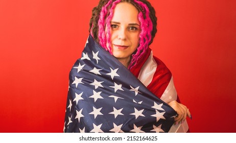 Young woman wrapped in American flag on red background. Happy female smiling and looking at camera, posing in studio. Concept of Flag Day, national holiday