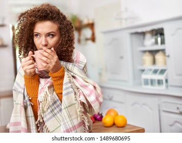 Young woman wrapped in blanket drinking hot tea 