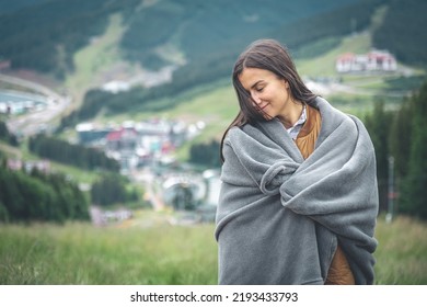 A young woman wrapped in a blanket in the mountains.