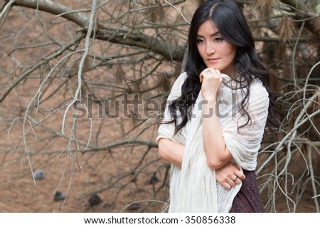 Young woman wrapped in a white scarf stays in brown forest