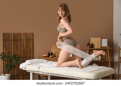 Young woman wrapping her leg with bandage on couch in spa salon - Powered by Shutterstock