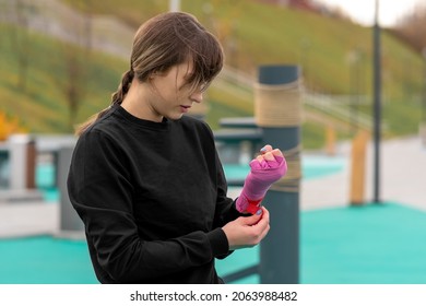 young woman wrapping a wrist wrap around her hand before outdoor martial arts training against the traditional training dummy - Powered by Shutterstock