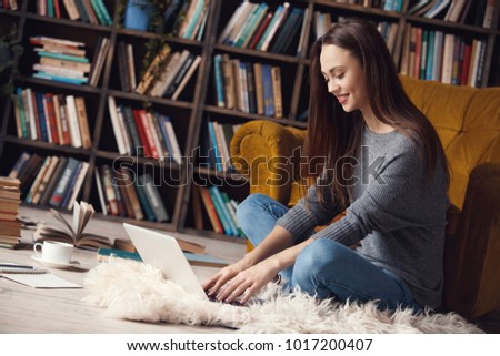 Young woman writer in library at home creative occupation sitting typing on laptop