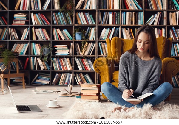 Young woman writer in library at home creative\
occupation sitting writing\
notes