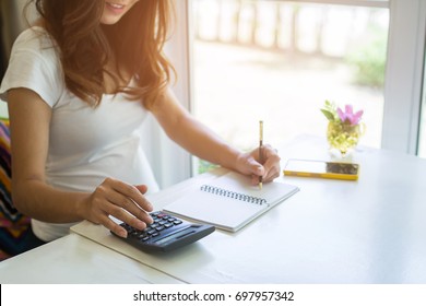Young woman writes to blank diary and using calculator on a white table at home.