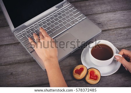 a young woman writes a text message on laptop keyboard with blank empty screen monitor, rest homes, people with a Cup of tea and a biscuit in the shape of a heart on wooden background