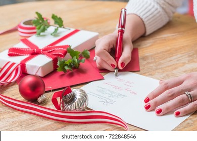 Young Woman Writing Christmas Cards With Red Nails, A Red Pen, And Holiday Decorations