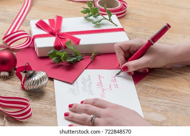 Young Woman Writing Christmas Cards With Red Nails, A Red Pen, And Holiday Decorations