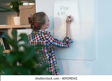 Young Woman Writing Day Plan On White Board, Holding Marker In Right Hand. Student Planning Schedule Rear View Portrait. 