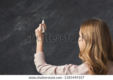 Young woman writing on blank wall, back view, copy space
