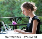 young woman writing on a white laptop computer on the balcony