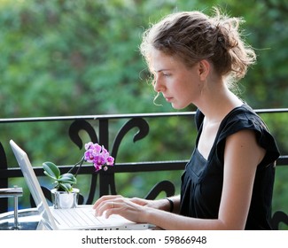 Young Woman Writing On A White Laptop Computer On The Balcony