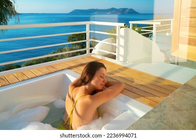 Young woman in yellow bikini relaxing in hot tub bath outside on luxury spa hotel resort
