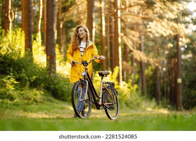 Young woman in yellow coat riding bicycle park. Active day.  - Powered by Shutterstock