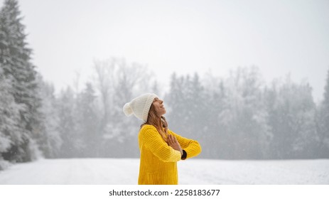 Young woman in yellow sweater with content peaceful expression on her face meditating with her palms joined in front of her chest. Standing outside in a wite snowy winter nature. - Shutterstock ID 2258183677