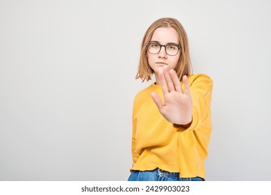 Young woman in yellow sweater and glasses making stop gesture with hand, on a light background. - Powered by Shutterstock