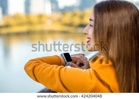 Young woman in yellow sweater using smart watch on the modern bridge with skyscrapers on the background. Sport application on the smart watch