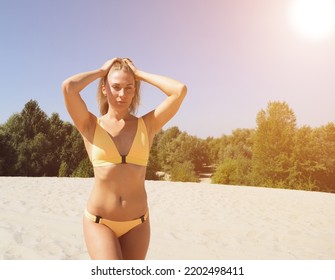 A Young Woman In A Yellow Swimsuit Holds Her Head With Her Hands While Standing On The Sand In The Desert. Sunshine Over Sand And Forest. Woman Relax In Summer