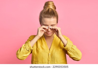 young woman in a yellow t-shirt on a pink background scratches her eyes - Shutterstock ID 2290353505