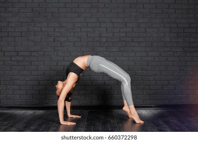 Young woman in yoga asana - bridge pose. Woman with long hair and slim body doing yoga exercise, stretching, Urdhva Dhanurasana. Healthy lifestyle. Woman do yoga indoors.