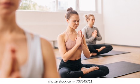 Young Woman In Yoga Class Doing Meditation Lotus Pose. Group Of Healthy People Meditating In A Yoga Studio.