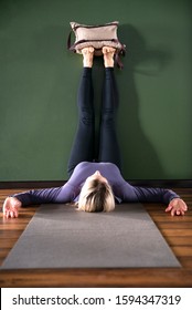 Young Woman In Yoga Relaxing Pose With Legs Up Against Wall With Heavy Sand Bags