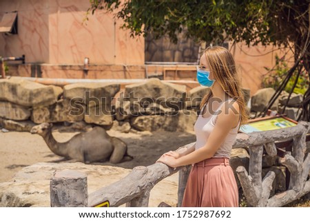 Young woman at the zoo in a medical mask. Visiting public places after the coronavirus epidemic