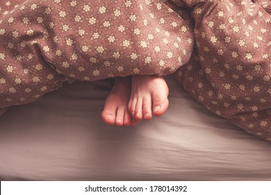 Young Woman's Feet In Bed Under The Covers