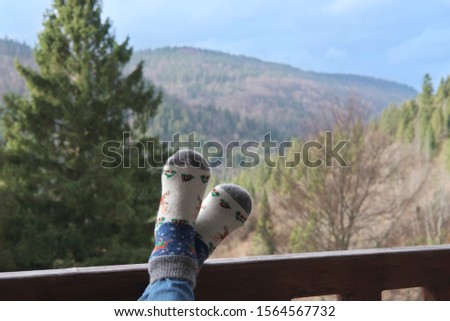 The young woman's feet laid on the wooden railing on the background of the mountains.