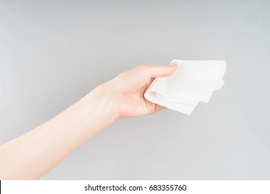 Young Woman's Or Girls Hand Giving A White Paper, Napkin Or Handkerchief, Isolated On Grey Background