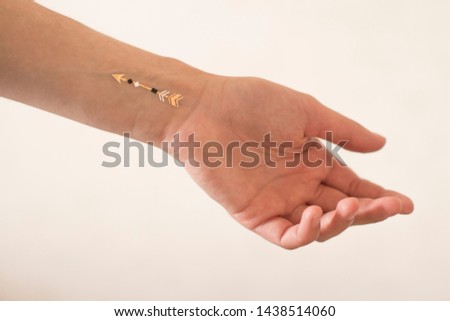 young woman's hand with gold arrow tattoo on her wrist on white background