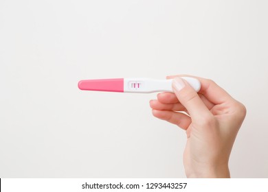 Young woman's hand holding pregnancy test with two stripes on gray background. Positive result. Closeup. Point view shot. Empty place for text.