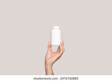 A young woman's hand holds a white plastic bottle isolated on a beige background. Mockup for branding a box with pills, capsules, pills, supplements or vitamins. Healthcare concept