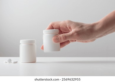 A young woman's hand holds a white plastic bottle on a white background. Mockup for branding a box with pills, capsules, pills, supplements or vitamins. Healthcare concept