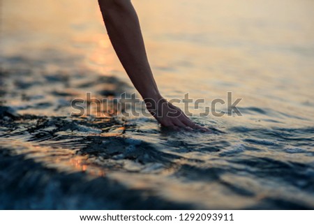 Young woman's hand touching the water in the sea