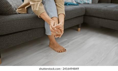 Young woman's hands massaging her tired feet, relaxed on the sofa at home's comforting interior