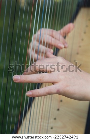 a young woman's hands playing the strings of a harp