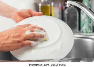 Young woman's hands washing a white dish with water and dish soap. Close-up of female hands rinsing a dirty and used dish with the faucet turned off. Concept of cleanliness