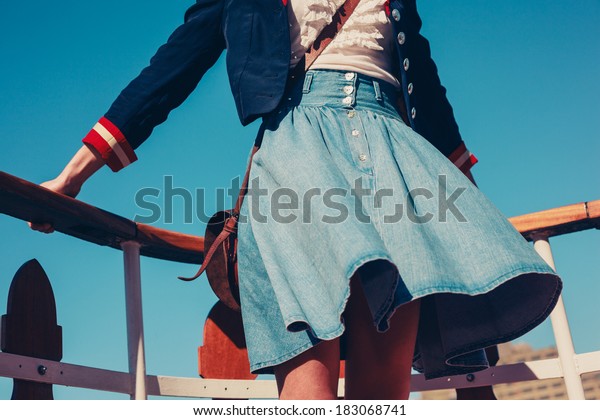 A young\
woman\'s skirt is blowing in the wind as she is standing on the deck\
of a boat cruising down the\
river