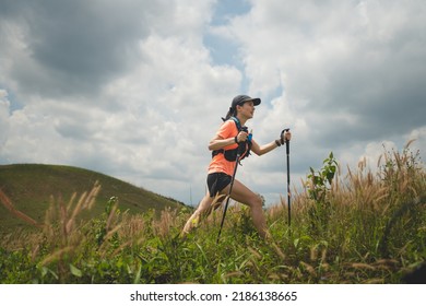 Young women active trail running across a meadow on a grassy trail high in the mountains in the afternoon with trekking pole