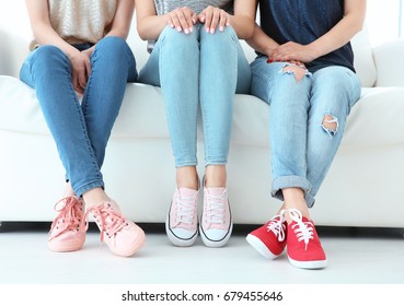 Young women with beautiful legs in jeans and sneakers sitting on sofa