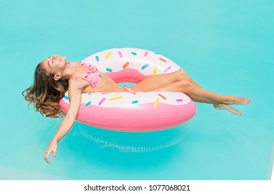Young women in bikini lying down on an inflatable donut in swimming pool. Girl enjoys sunbathing on floating pool inflatable toy on hot summer day