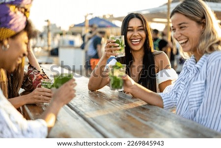 Young women celebrating at beach chiringuito, focus on brunette woman with toothy smile